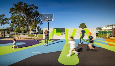 Image of Syd Jones Reserve in the City of Norwood Payneham & St Peters in South Australia, with children playing basketball and riding scooters, and a person walking a dog